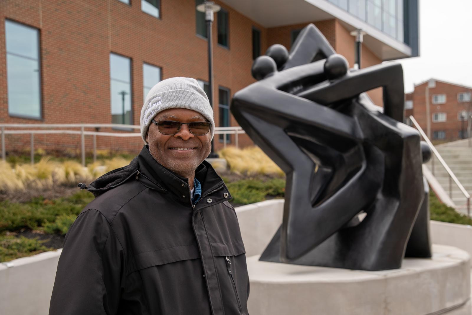 Nnamdi Okonkwo smiling in front of Community of Stars sculpture