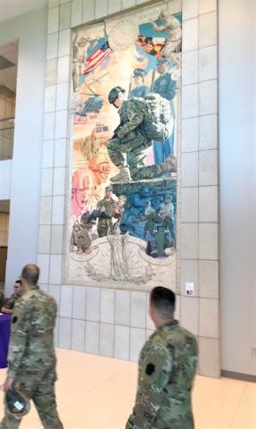 Two soldiers walking by a mural depicting a scene with soldiers 
