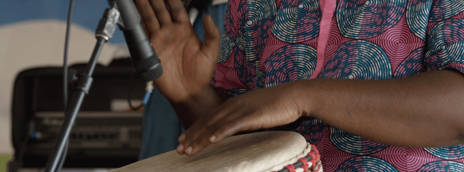 Close up of dark skinned hands beating a drum at an outdoor event