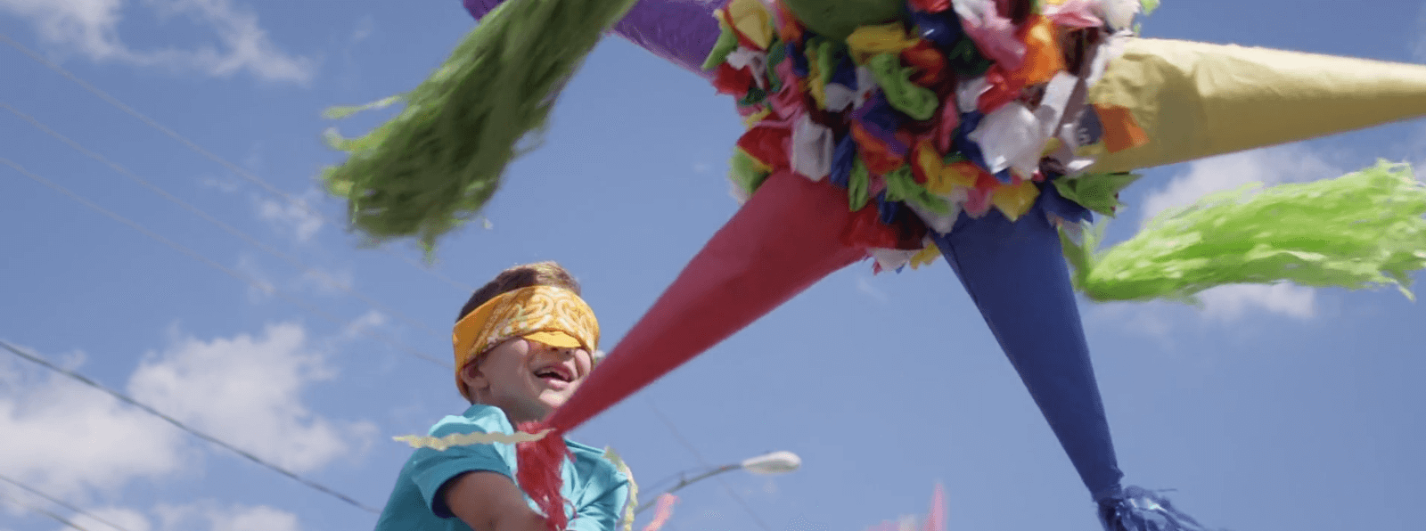 A blindfolded child swings at a colorful pinata outdoors