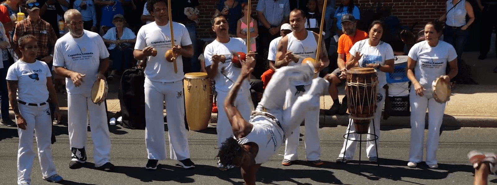 A dancer doing a flip in front of a group of other dancers who are gathered around playing instruments