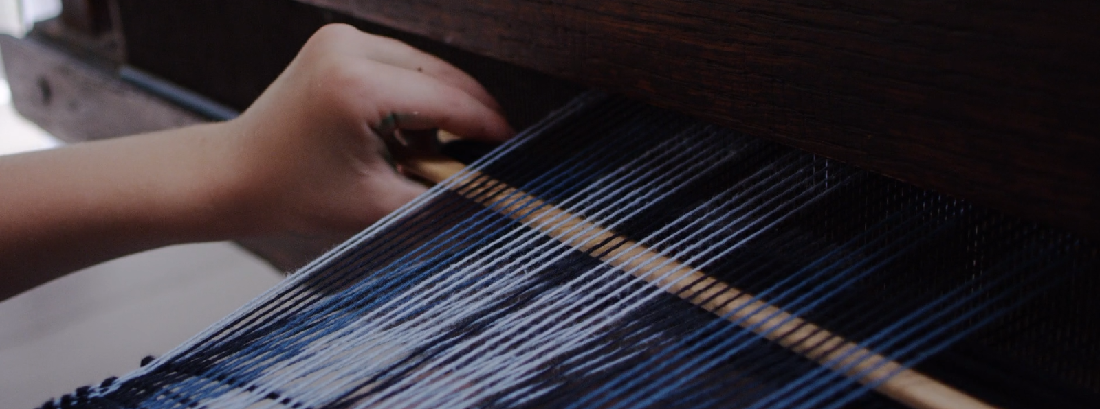 Close up of a child&#039;s hand weaving on a loom.