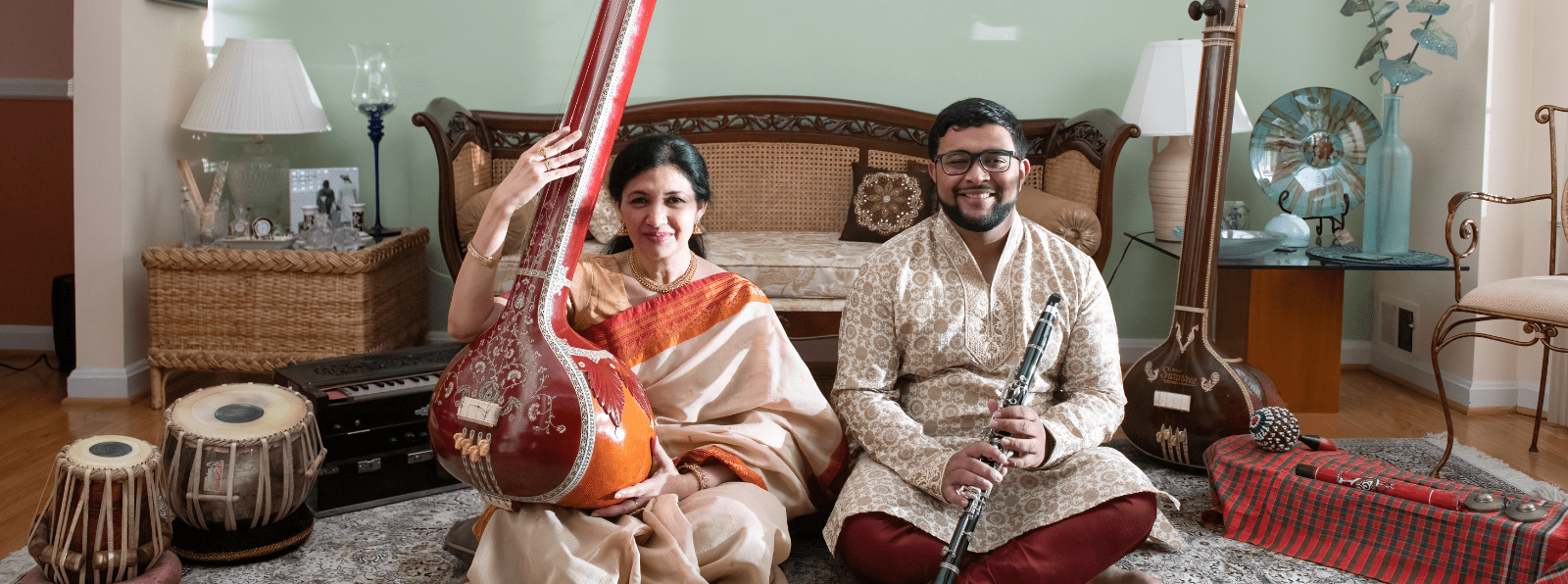 A man and a woman sit on the floor holding instruments