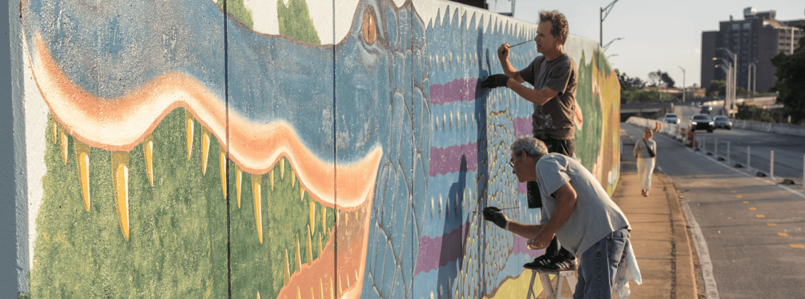 two artists conserving a public art mural in baltimore city.