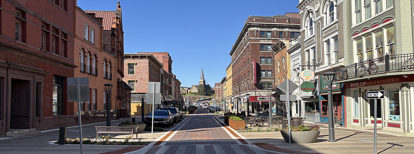 Cumberland Arts District header image. Empty street with buildings and cars along both sides, church building at end of road.