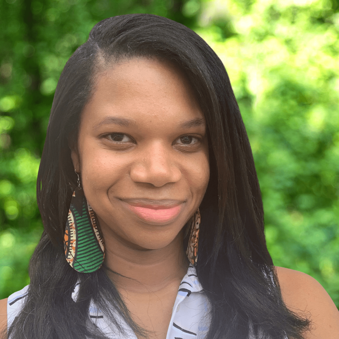 Women with long straight dark hair, grinning in a selfie with a blue collared top and large Kente cloth earrings. 