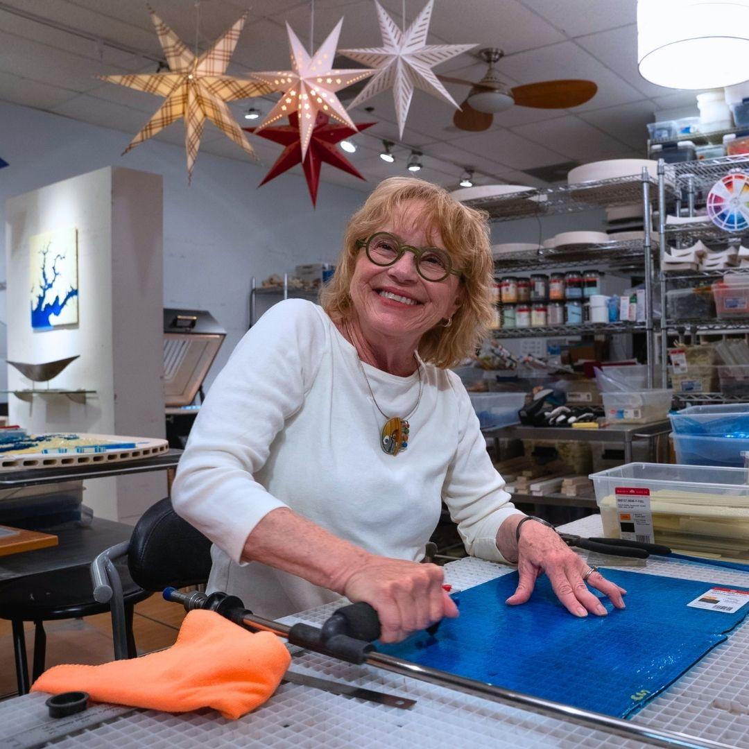 Smiling woman with glasses preparing to cut glass in her Kent County studio.