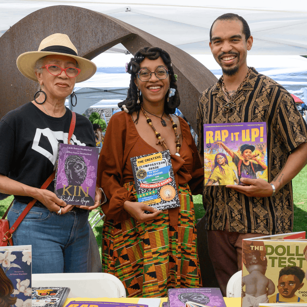 two woman and a man stand posed smiling with a book in each of their hands