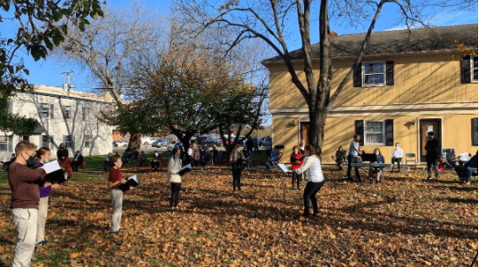 Group of people standing distanced outdoors singing