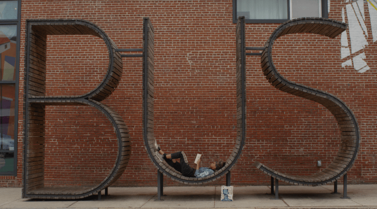 Person laying and reading on a BUS public art piece