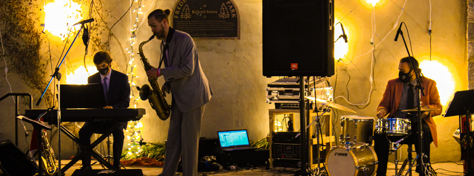 A pianist, saxophone player, and a drummer are performing in front of a wall of lights.