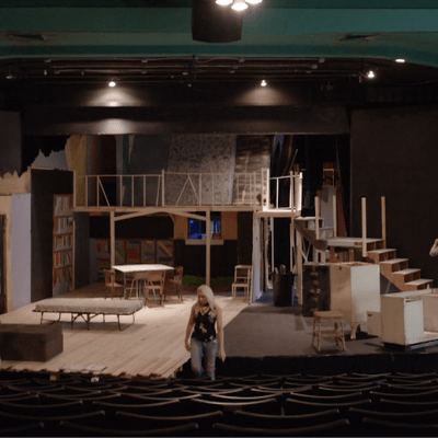 Four people working on a stage setting up a play in an empty theater