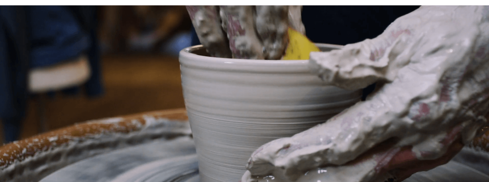 Two hands covered in clay molding on a pottery wheel