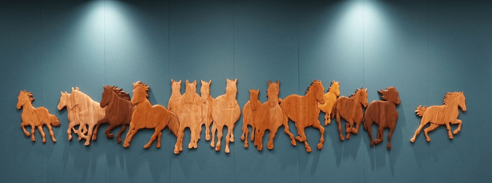 A wood sculpture displayed against the wall of galloping horses.