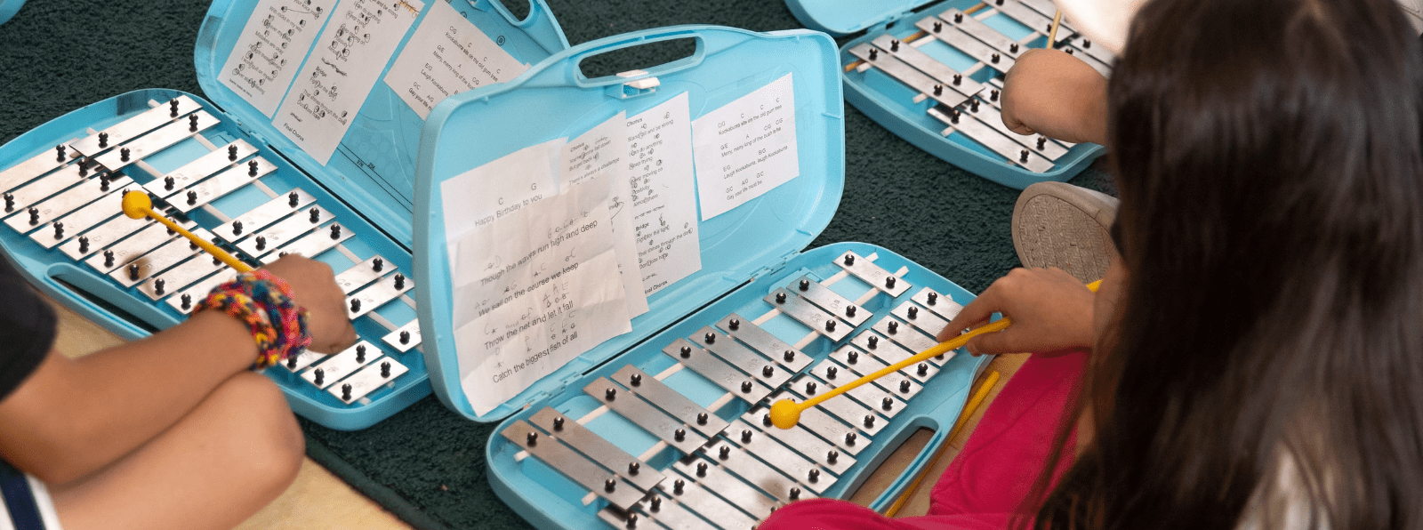 Closeup of three children playing the xylophone.