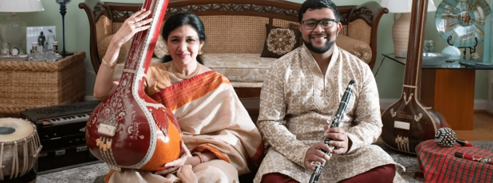 A man and a woman sit on the floor holding instruments